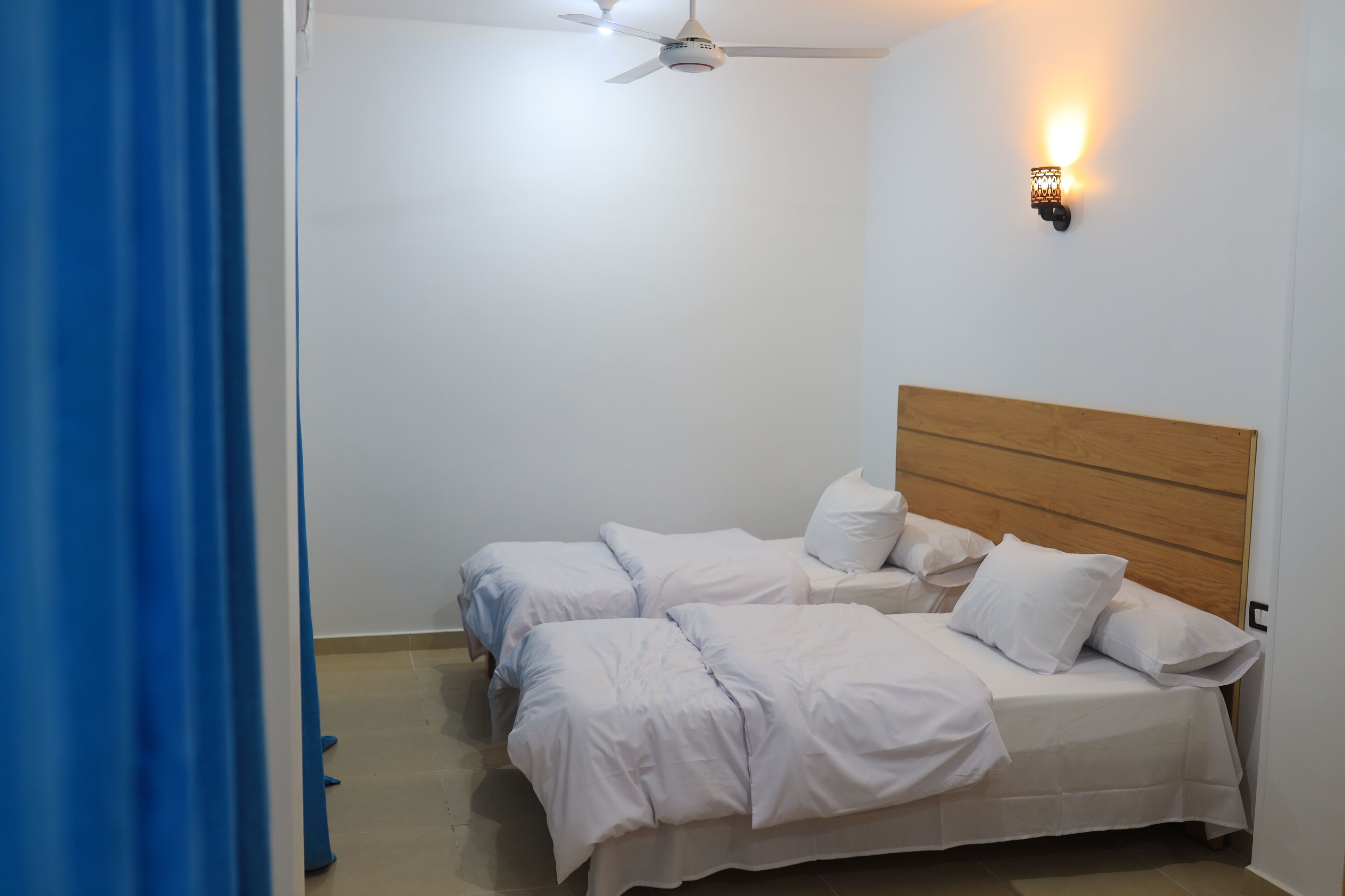 A bedroom with two beds, a ceiling fan, and a wall-mounted light fixture.