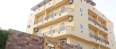 A multi-story building with balconies, a stone wall entrance, and a sign reading "ROYAL MOUNTAIN".