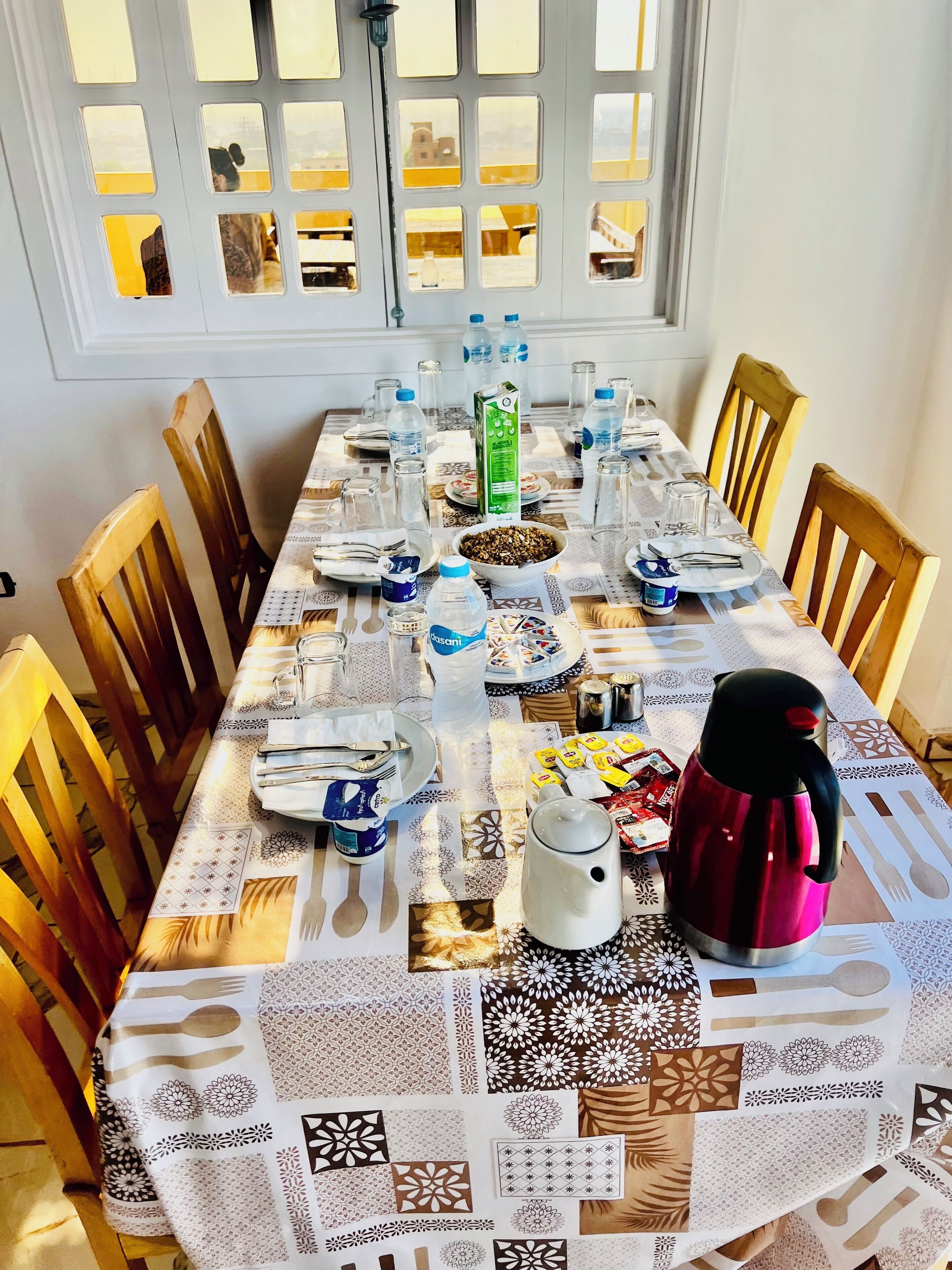 Una mesa de comedor con platos, cubiertos, vasos y una termo.