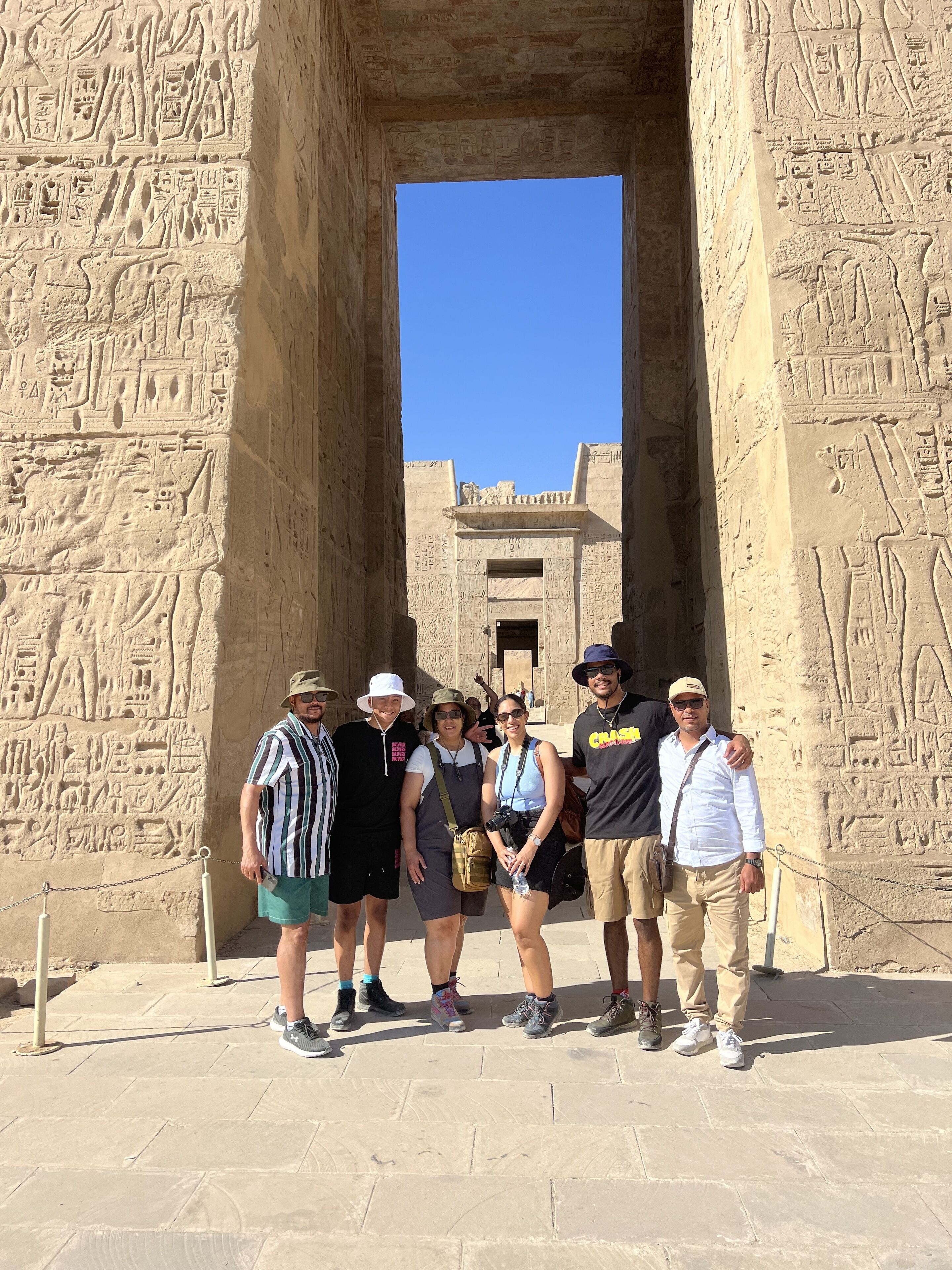 Un groupe de personnes se tient devant une porte d’un ancien temple égyptien, ornée d’hiéroglyphes.