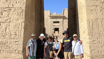 Un groupe de personnes se tient devant une porte d’un ancien temple égyptien, ornée d’hiéroglyphes.