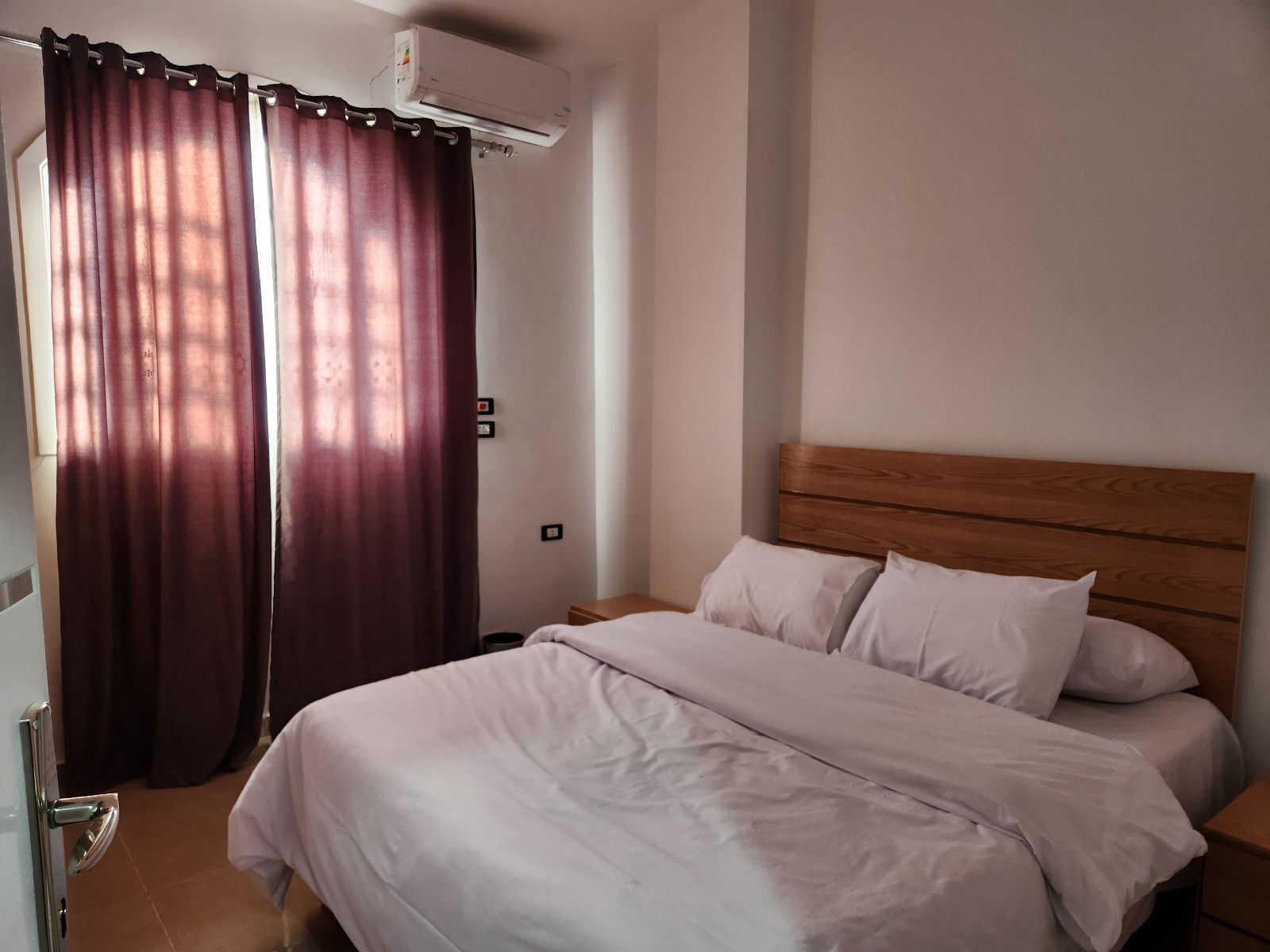 A bedroom with a wooden headboard, white bedding, and a large window with curtains.
