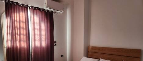 A bedroom with a wooden headboard, white bedding, and a large window with curtains.