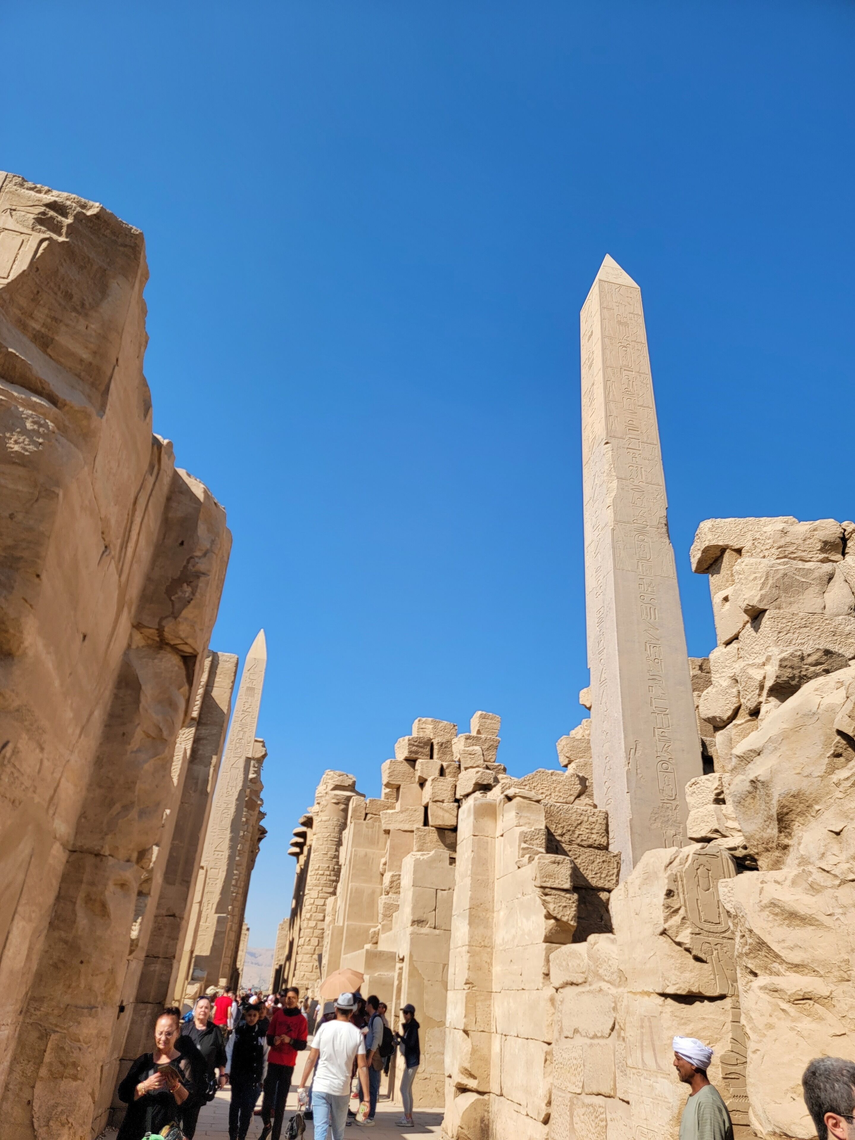 A corridor with ancient stone columns and hieroglyphs, lined with tourists.