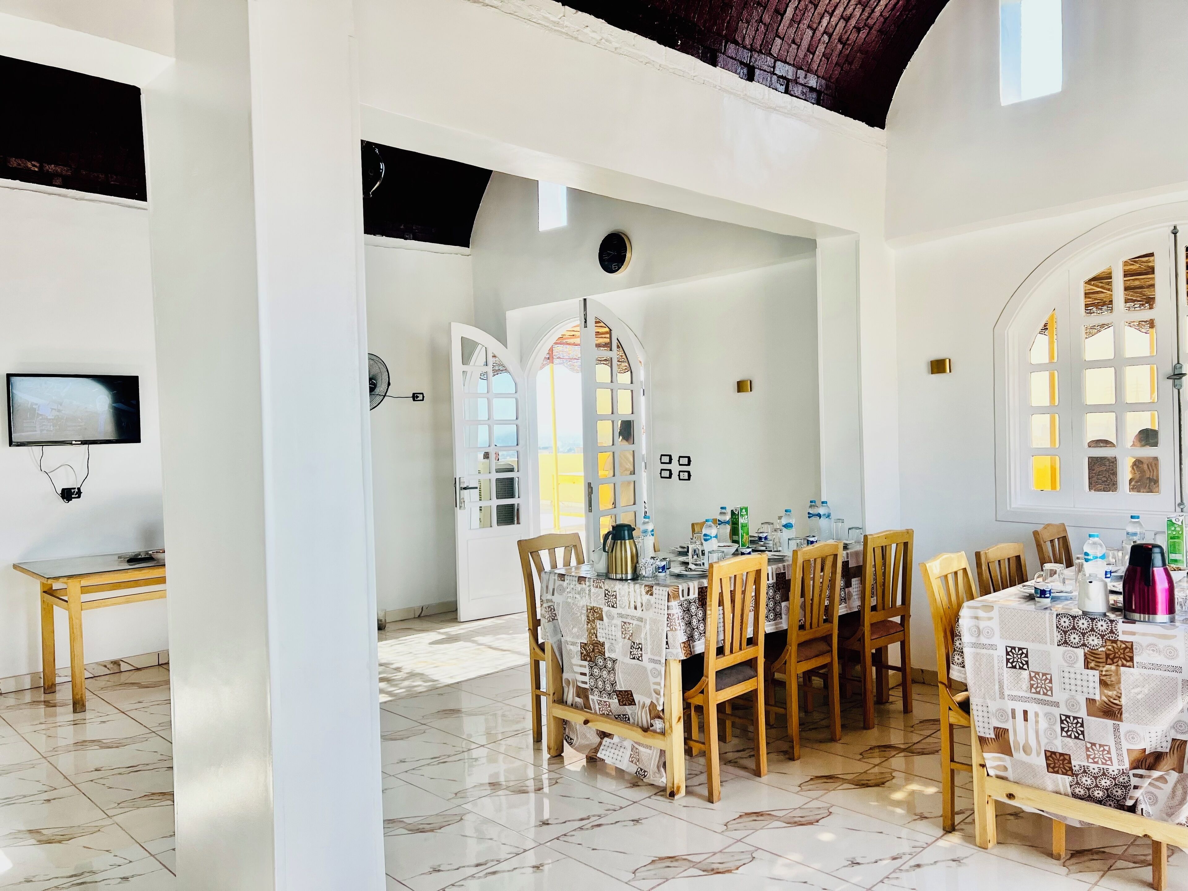 A dining area with a large table set for multiple people, a television on the wall, and a clock on the wall.
