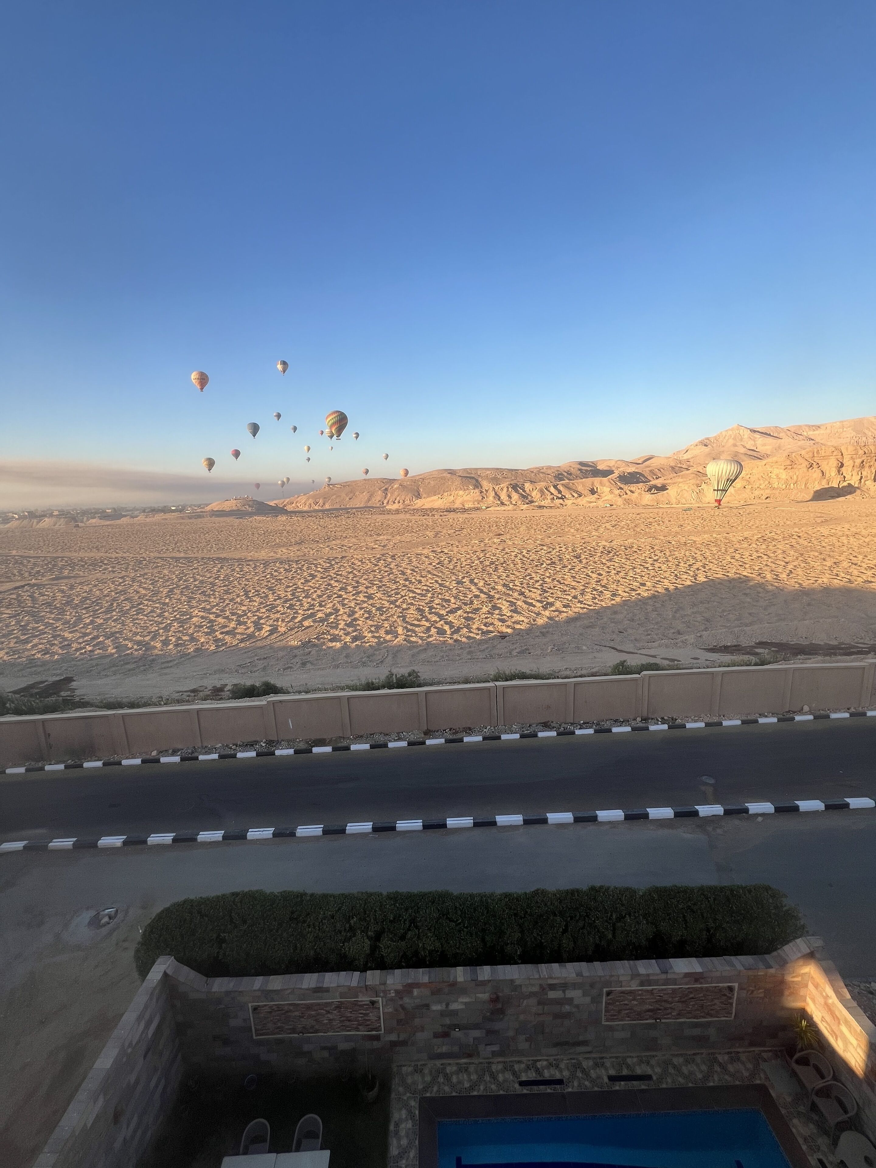 A desert landscape with hot air balloons and a road in the foreground.