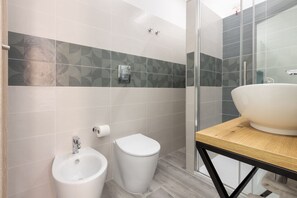 A modern bathroom with a bidet, toilet, and a large sink with a wooden countertop. - DELEDDA HOME (Cagliari)