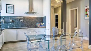 A modern kitchen with a glass dining table and chairs, a stainless steel range hood, and a framed family rules poster on the wall. - Beautiful 120m2 Flat in bourgeois building with terrace (Cannes)