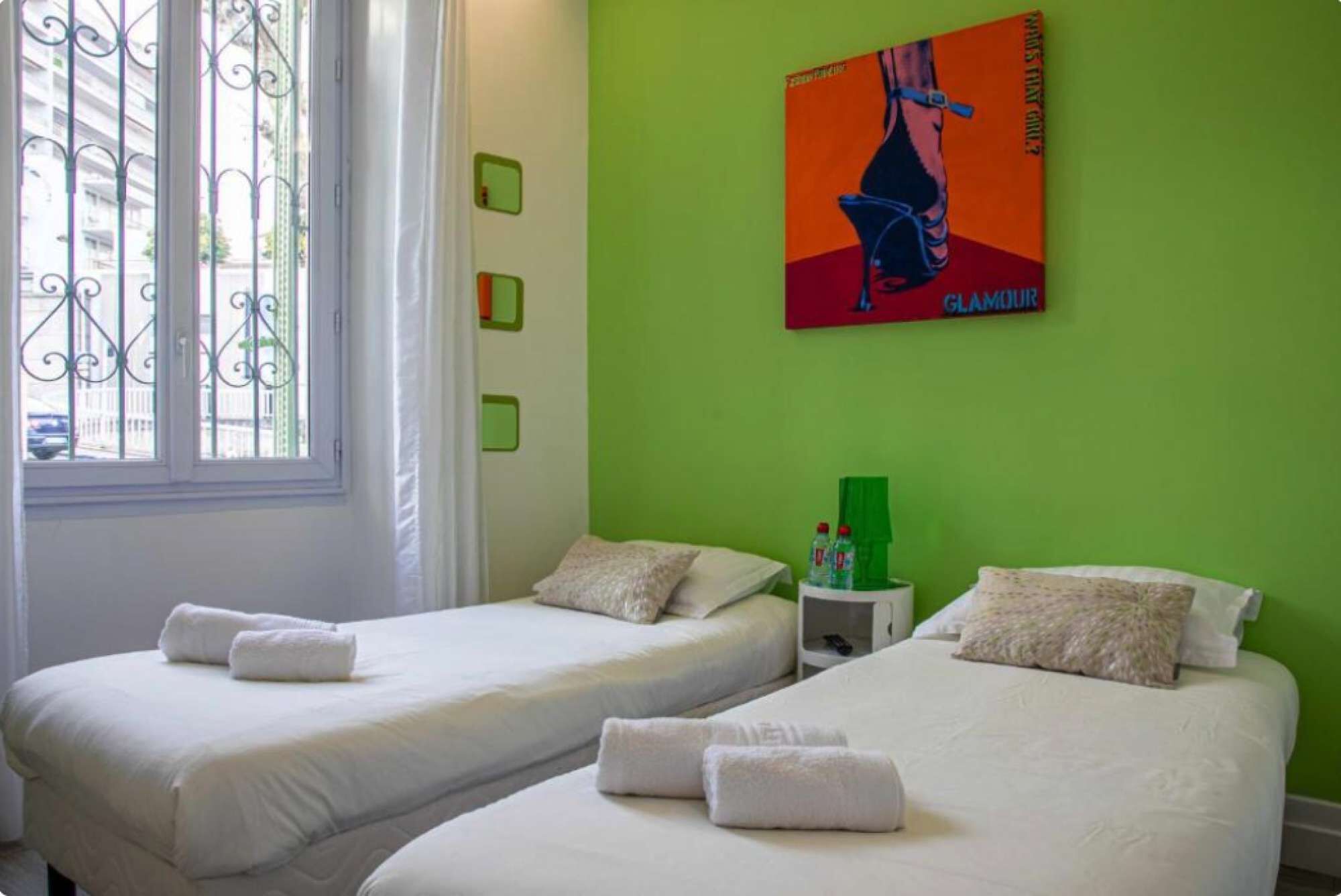 Een hotelkamer met twee bedden, een raam met metalen tralies, een groene muur en een poster.