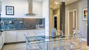A modern kitchen with a glass dining table and chairs, a stainless steel range hood, and a framed family rules poster on the wall.
