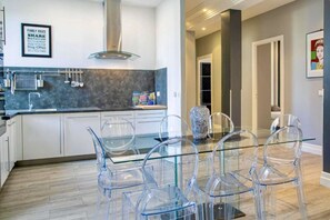 A modern kitchen with a glass dining table and chairs, a stainless steel range hood, and a framed family rules poster on the wall.