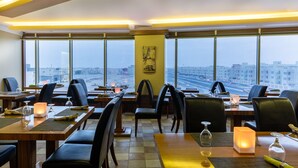 Un restaurant doté de nombreuses tables, de chaises et offrant une vue sur le paysage urbain grâce à de grandes fenêtres.