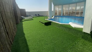 Un espace piscine aménagé sur le toit, avec du gazon synthétique, des chaises longues et une piscine à l’eau d’un bleu limpide.