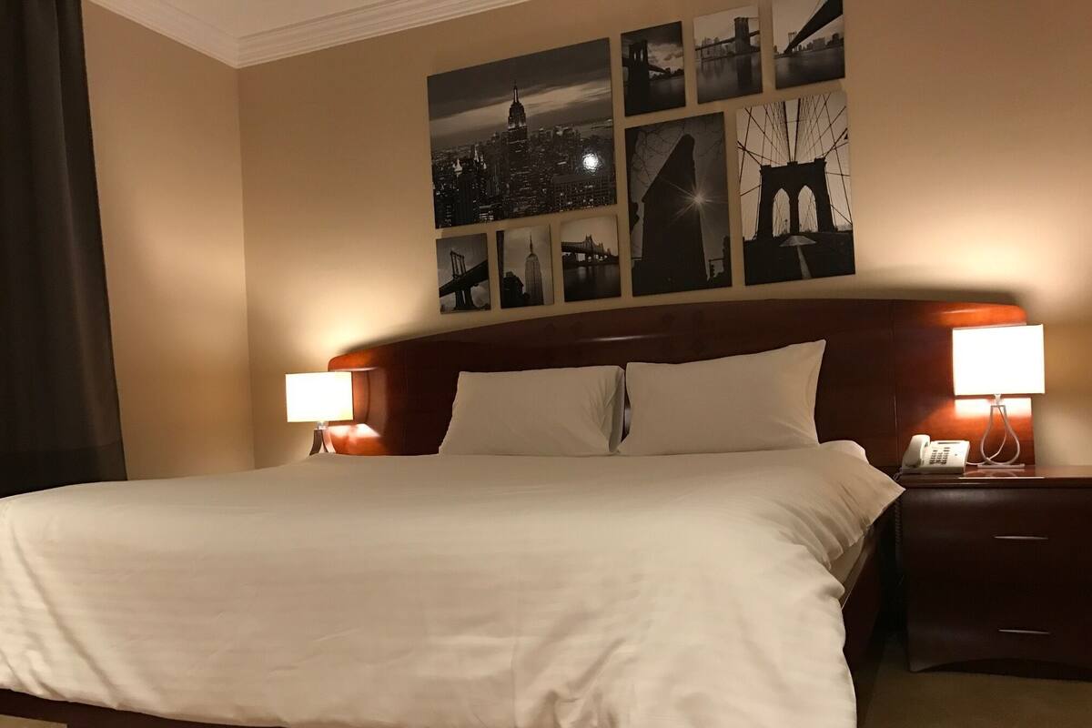 A hotel room with a large bed, two bedside tables with lamps, and a wall decorated with cityscape photographs.