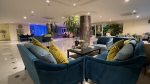 Un hall d’entrée spacieux, avec des fauteuils bleus, une table basse et une grande colonne.