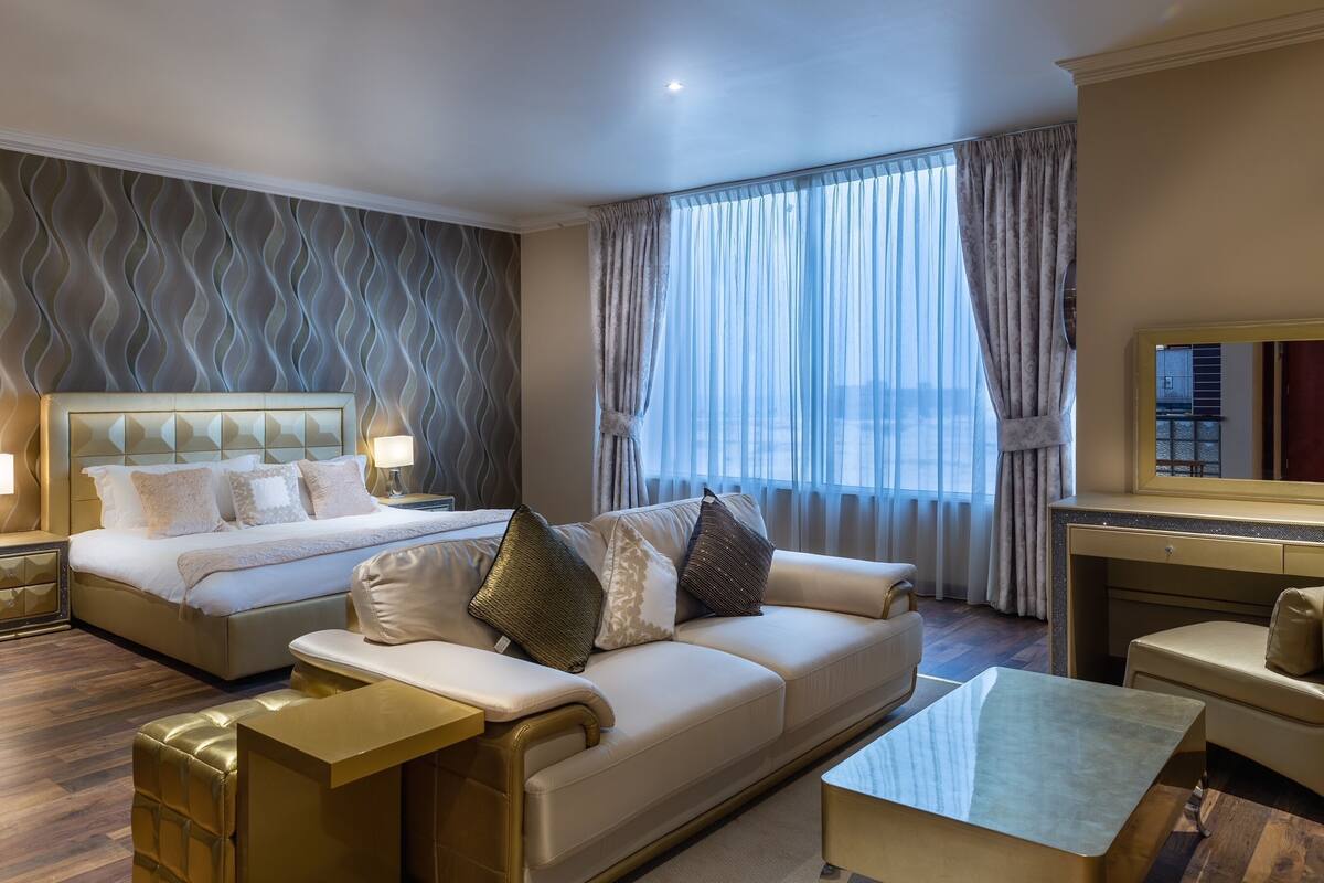 A hotel room with a bed, a sofa, a coffee table, a TV, and a large window with curtains.