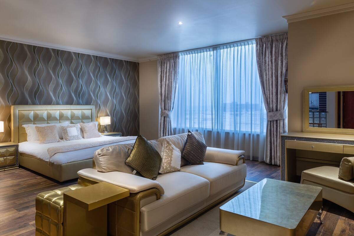A hotel room with a large bed, a sofa, a coffee table, and a TV.