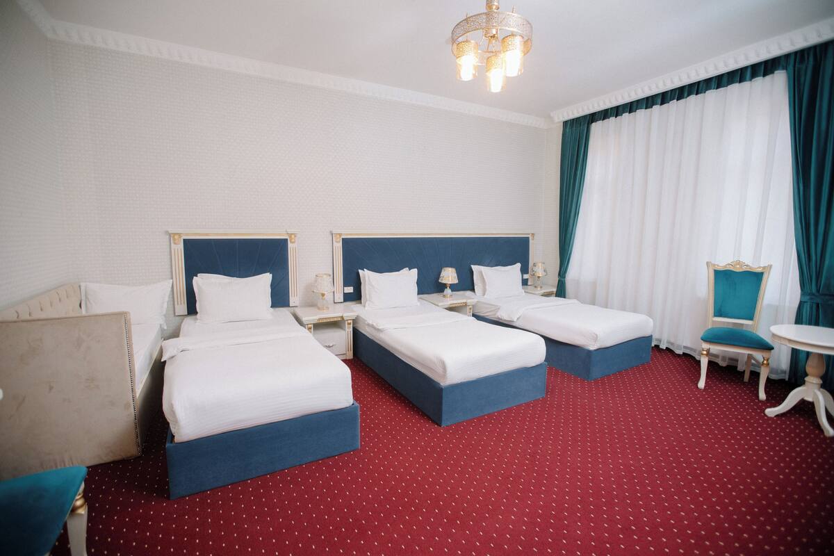 A hotel room with two beds, a chair, a table, and a chandelier.