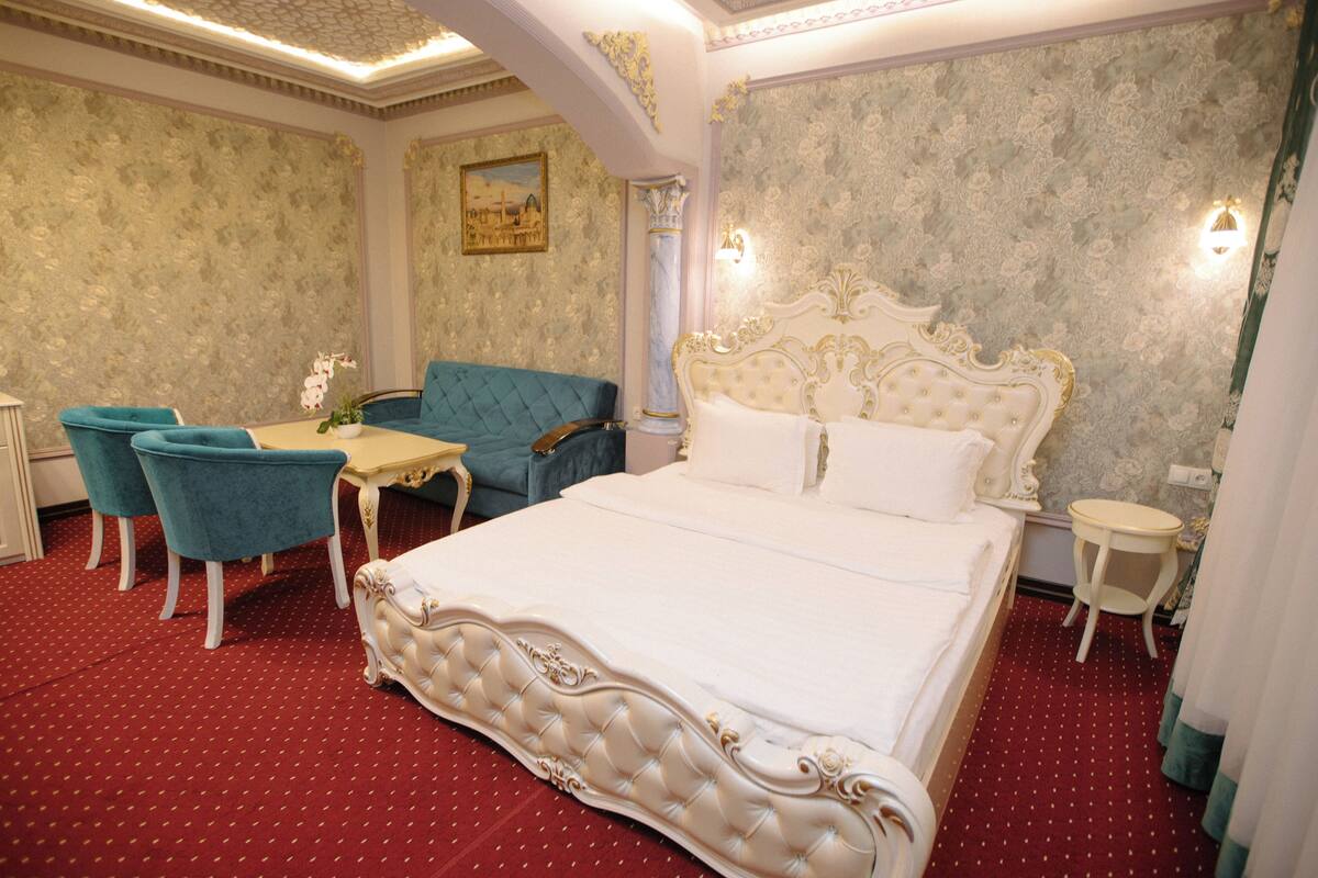 A hotel room with a large bed, a sofa, two chairs, a small table, and a nightstand.