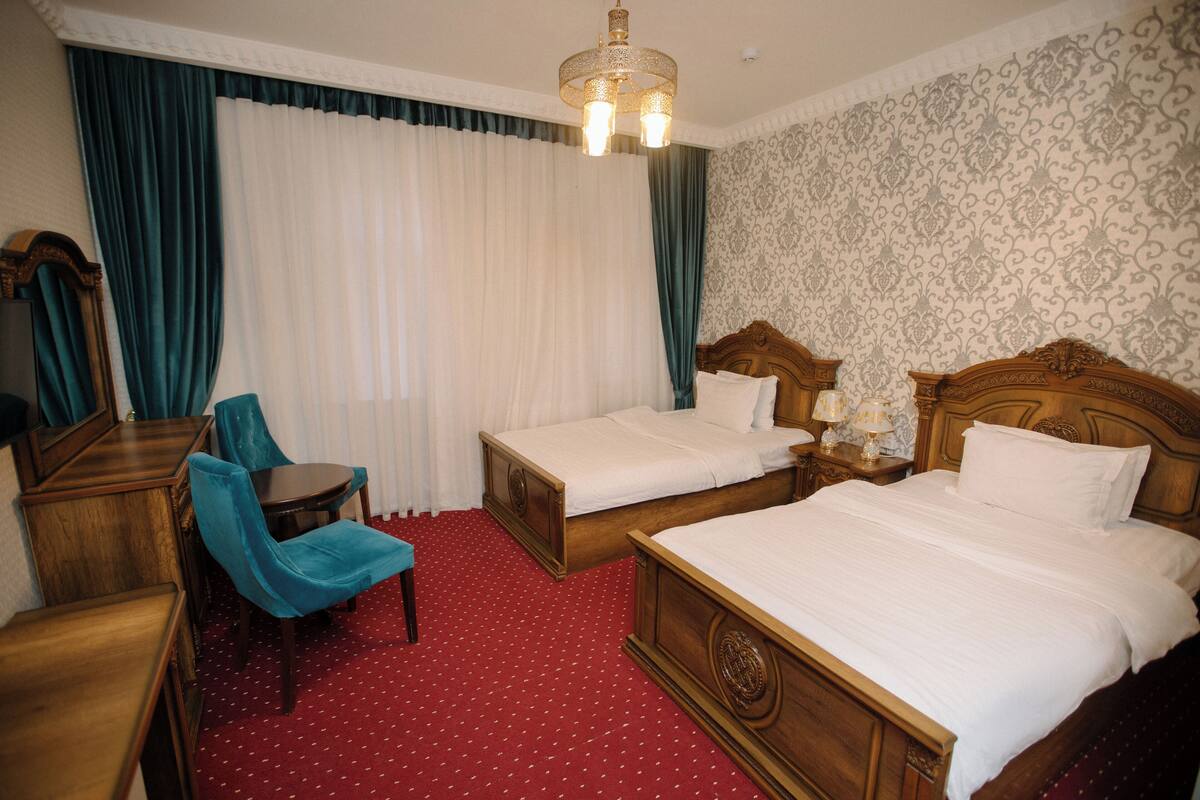 A hotel room with two single beds, a wooden dresser, a blue chair, and a red carpet.