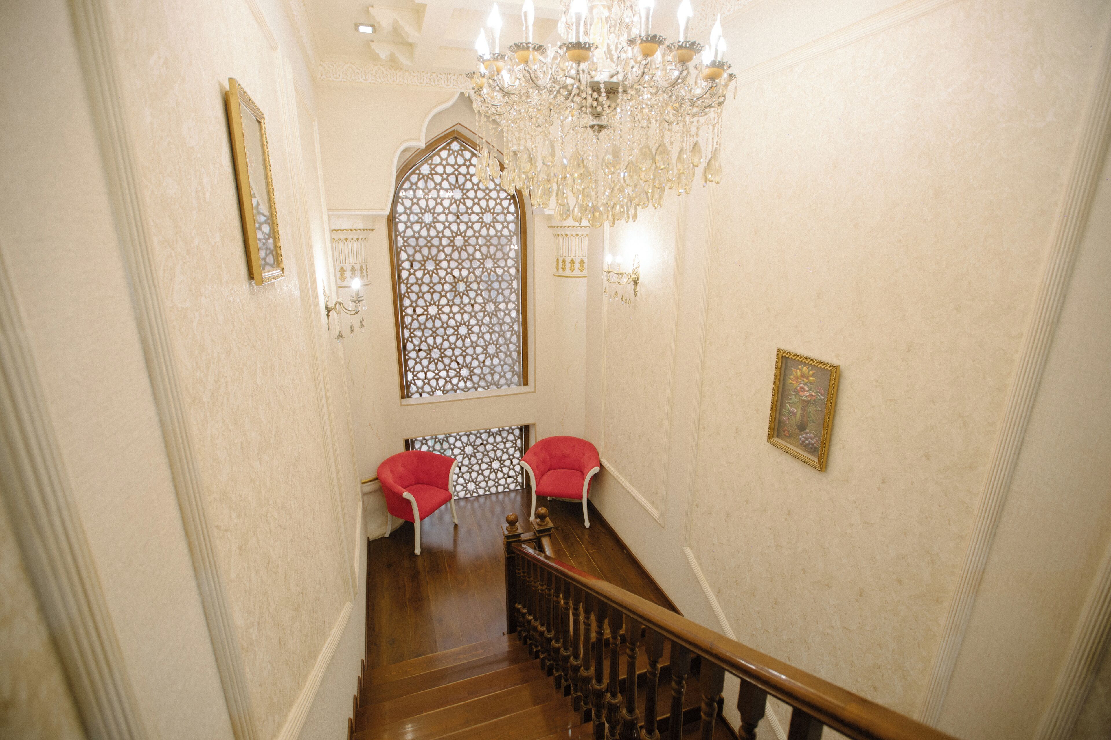 A grand staircase with a wooden handrail, a chandelier, and two red chairs at the bottom.