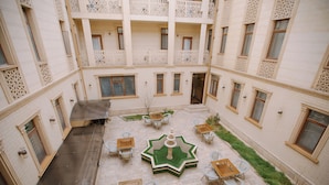 A courtyard with a central fountain, surrounded by tables and chairs, and balconies on the upper floors. - Dendi Plaza (Bukhara)