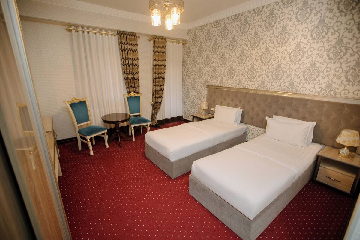 A hotel room with two beds, a small table, two chairs, a nightstand, and a chandelier.