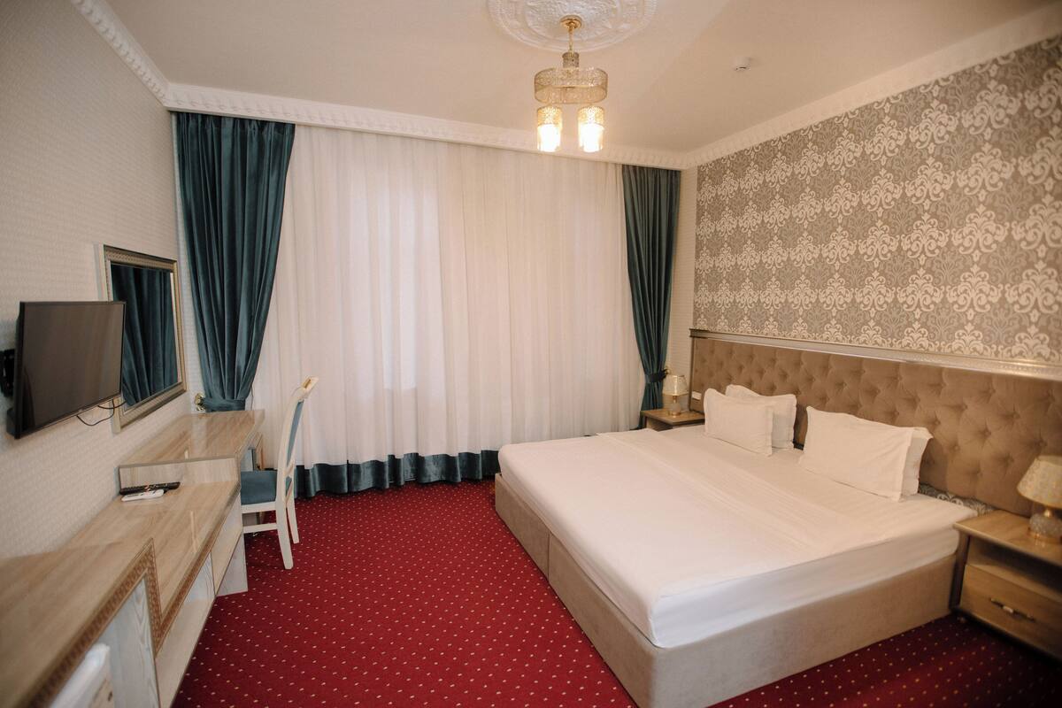 A hotel room with a large bed, a desk with a chair, a television, and a chandelier.