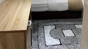 Une chambre moderne avec un bureau en bois, un lit recouvert d’une couverture beige et un tapis à motifs.