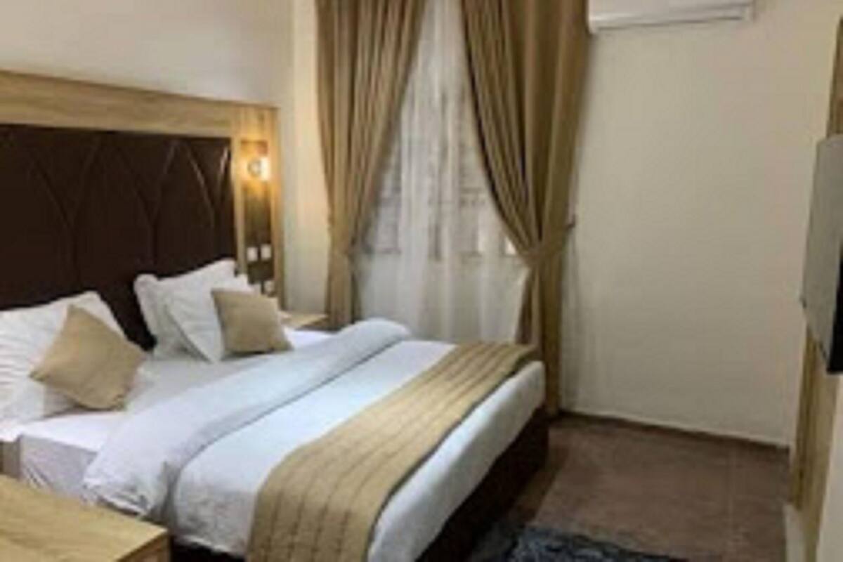 A hotel room with a bed, a bedside table, a lamp, and a window with curtains.