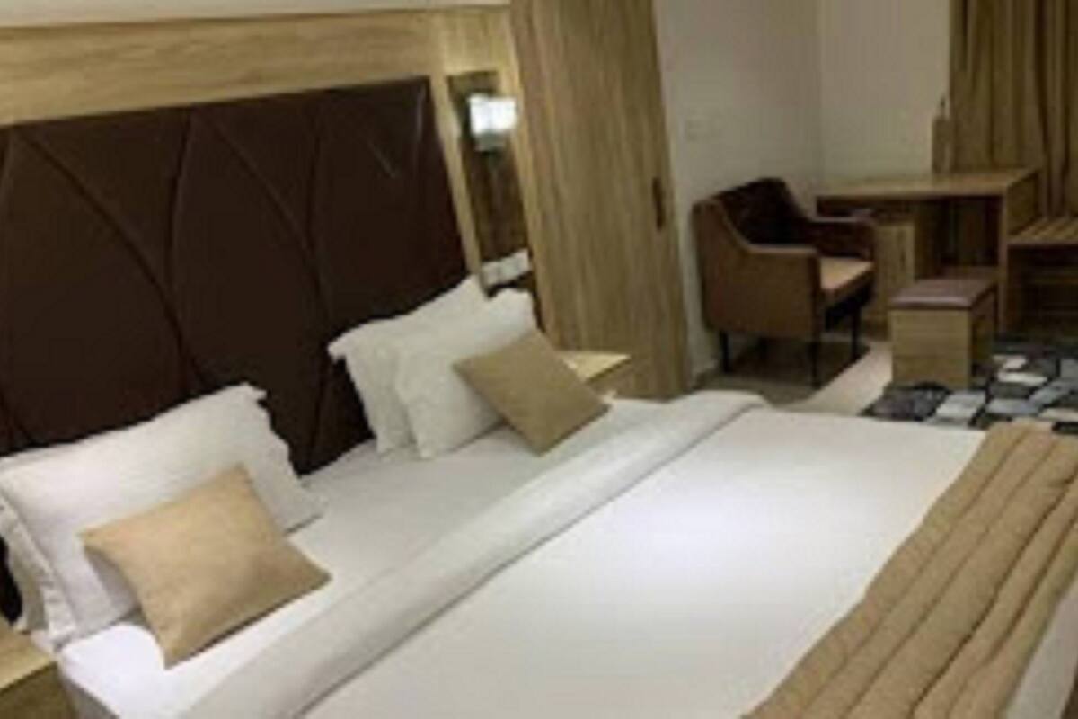 A hotel room with a large bed, a wooden headboard, a desk, and a chair.