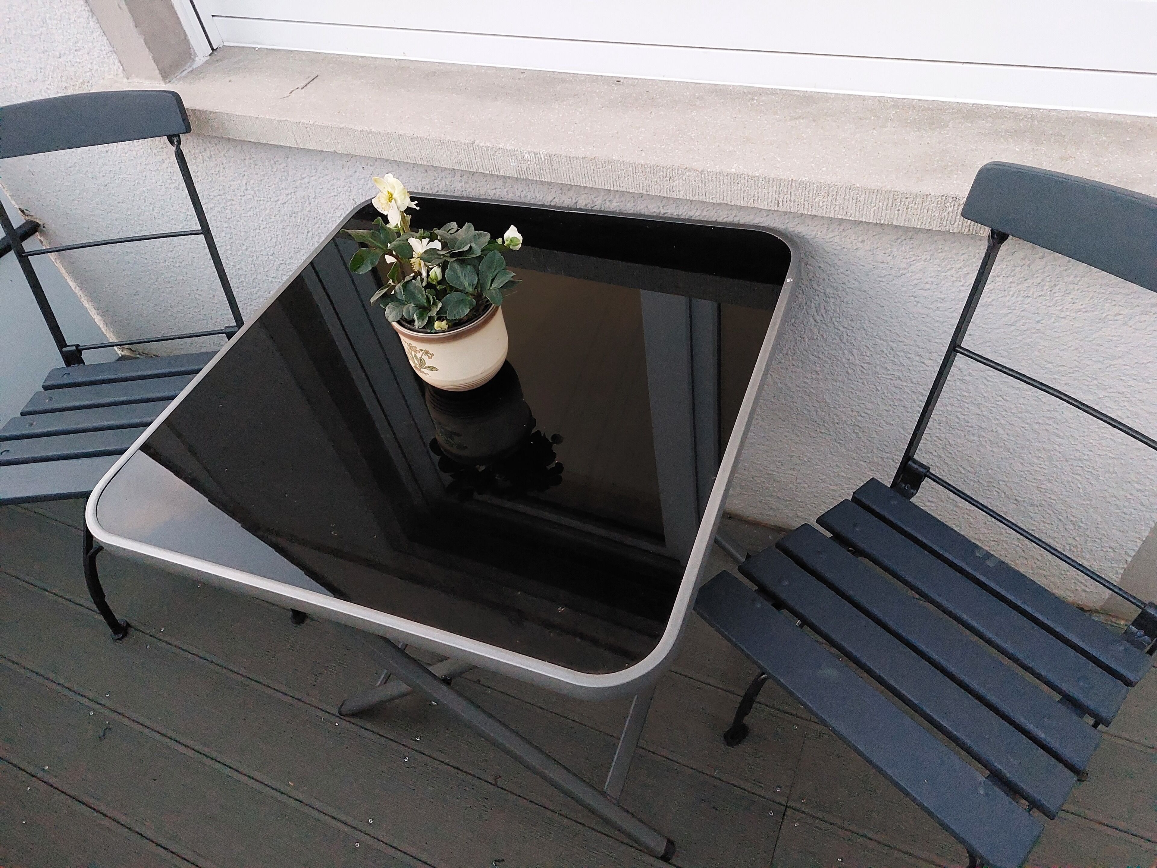 A small outdoor table with a potted plant on it, positioned between two metal chairs.