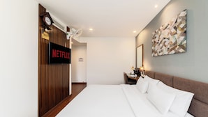 A modern hotel room with a large bed, a wall-mounted TV displaying 'NETFLIX', a clock, and a wooden panel wall. - A25 Premium Hotel - 55 Cach Mang Thang 8 (Ho Chi Minh City)