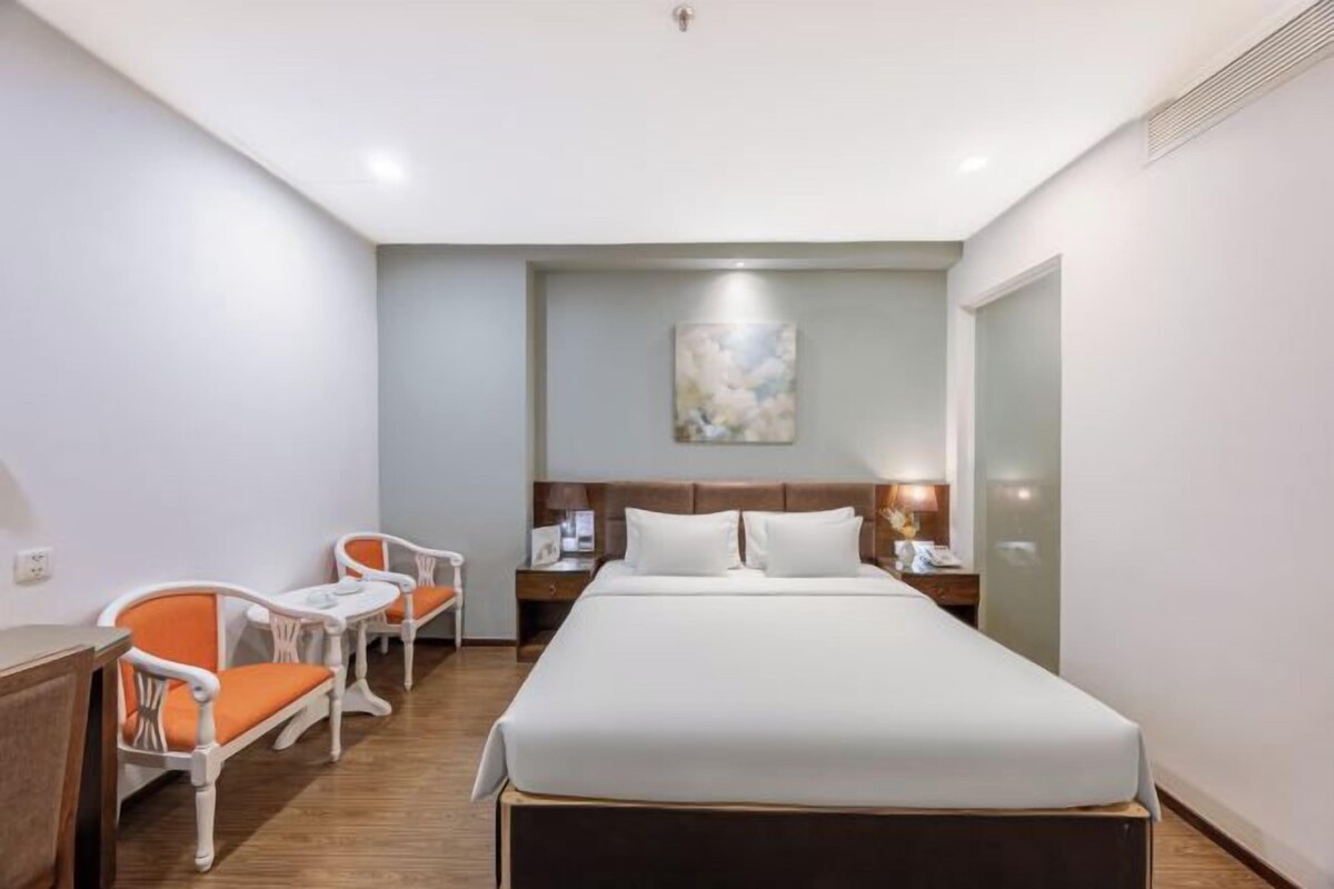 A hotel room with a bed, two chairs, a nightstand, and a painting on the wall.