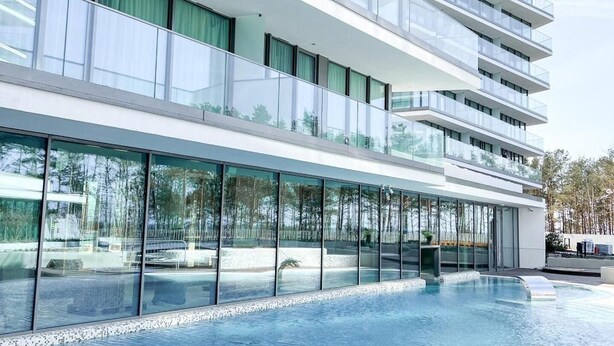 A modern hotel with multiple balconies, large glass windows, and a swimming pool area. - Apartament Morski Widok (Miedzyzdroje)
