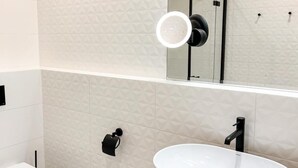 A modern bathroom with a white sink, wooden vanity, and a mirror with a light. - Apartament Morski Widok (Miedzyzdroje)