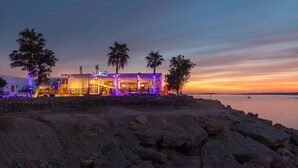 A seaside restaurant with a stone facade, illuminated by colorful lights, and palm trees in the background. - Albatros Sharm Resort - By Pickalbatros (Sharm El Sheikh)