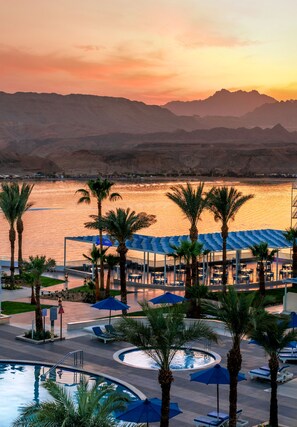 A resort pool area with palm trees, lounge chairs, and umbrellas, overlooking a body of water and mountains. - Albatros Sharm Resort - By Pickalbatros (Sharm El Sheikh)