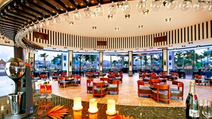 A spacious restaurant with a circular layout, multiple seating areas, and a view of palm trees through large windows. - Albatros Sharm Resort - By Pickalbatros (Sharm El Sheikh)
