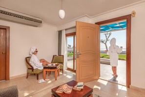 A hotel room with a large wooden door, a sitting area with a chair and a table, and a view of the outdoors through the door. - Albatros Sharm Resort - By Pickalbatros (Sharm El Sheikh)