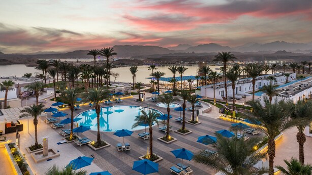 A resort pool area with palm trees, lounge chairs, and umbrellas. - Albatros Sharm Resort - By Pickalbatros (Sharm El Sheikh)