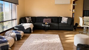 A modern living room with a sectional sofa, a small side table, a white ottoman, a large beige rug, and a glass coffee table. - Pelicans Rest Albany, 5 min to the beach, 6 min to city. Great all year round! (Collingwood Park)