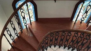 A spiral staircase with a wooden finish and black wrought iron railing, leading to a room with a tiled wall and a black chair. - Palazzo Excelsus  (Terzigno)