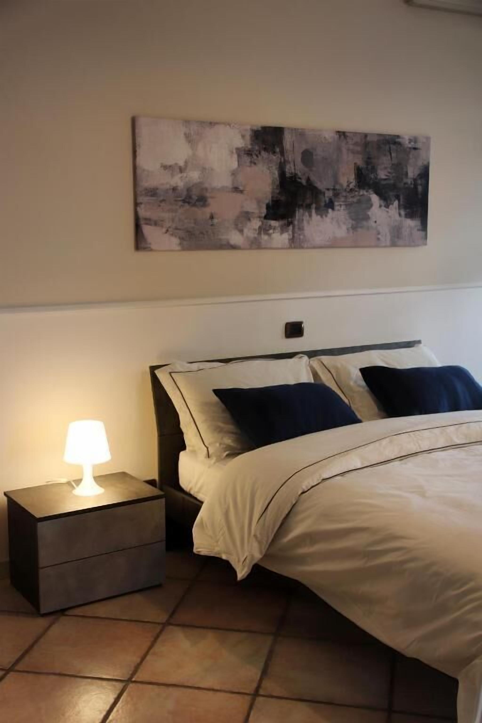 A bedroom with a bed, nightstand, and a wall-mounted abstract painting.