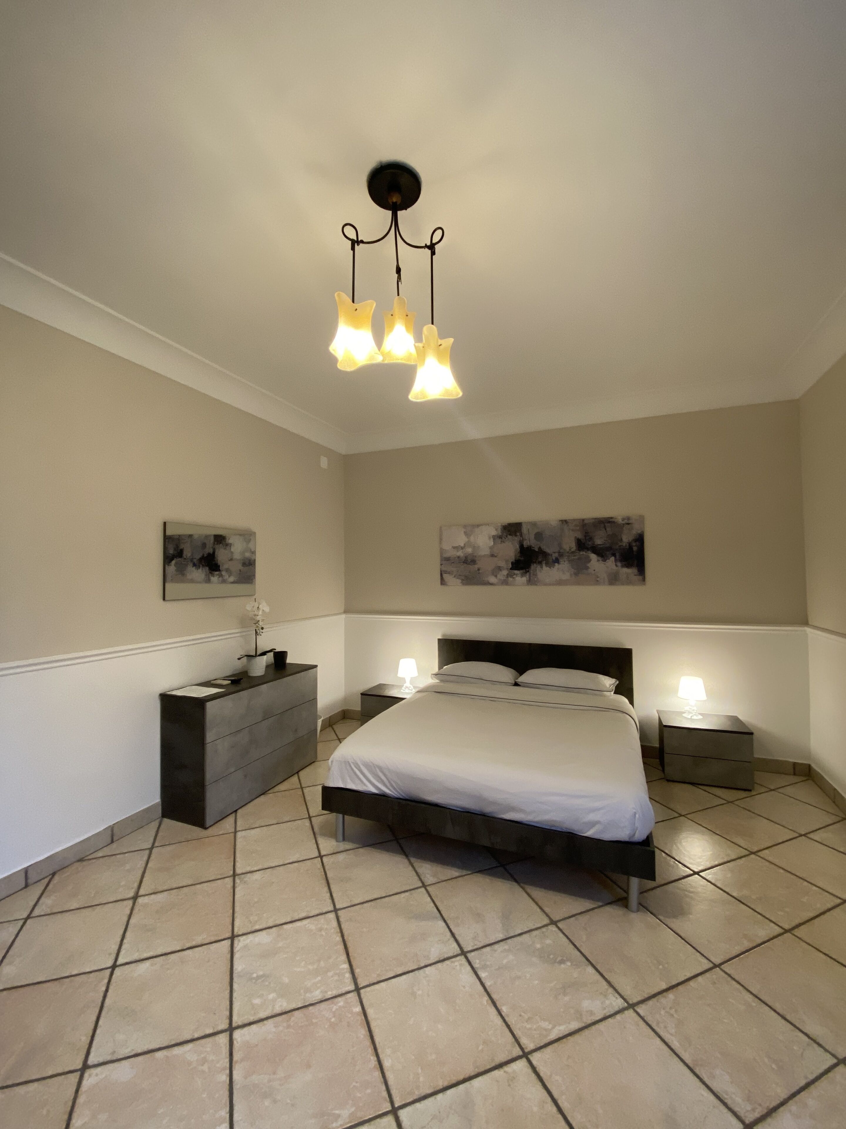 A bedroom with a bed, bedside tables, a dresser, and two wall-mounted paintings.