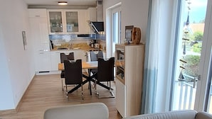 Een moderne woonkamer met een beige bank, uitzicht op de keuken en een eethoek.