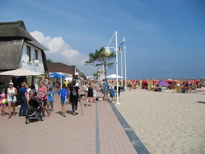A beachside promenade with shops, a thatched-roof building, and beach umbrellas.