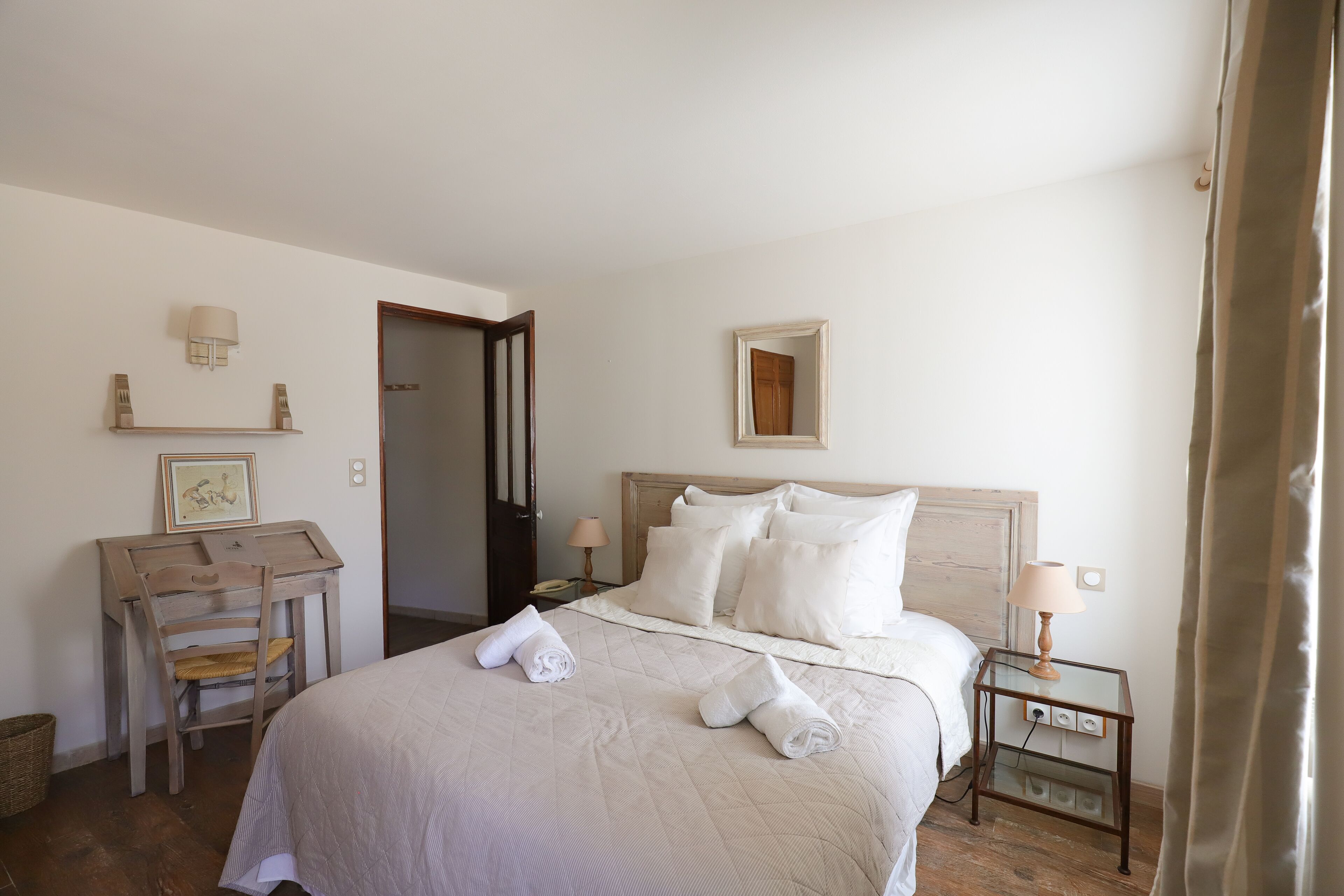A neatly arranged hotel room with a bed, a desk, a chair, a nightstand, and a mirror.