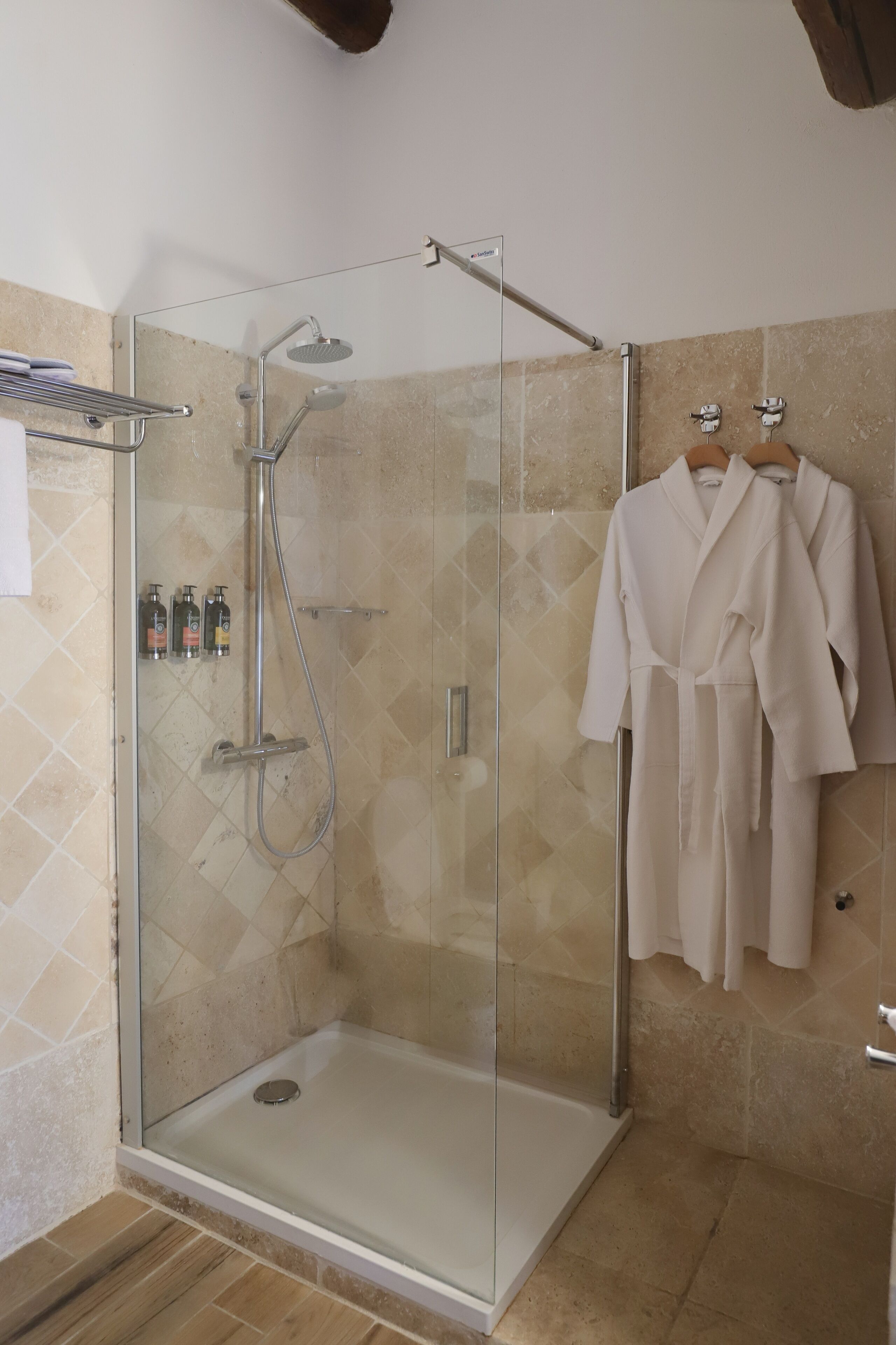 Une douche fermée par des parois en verre, dotée d’un pommeau de douche à main et d’un robinet mural.