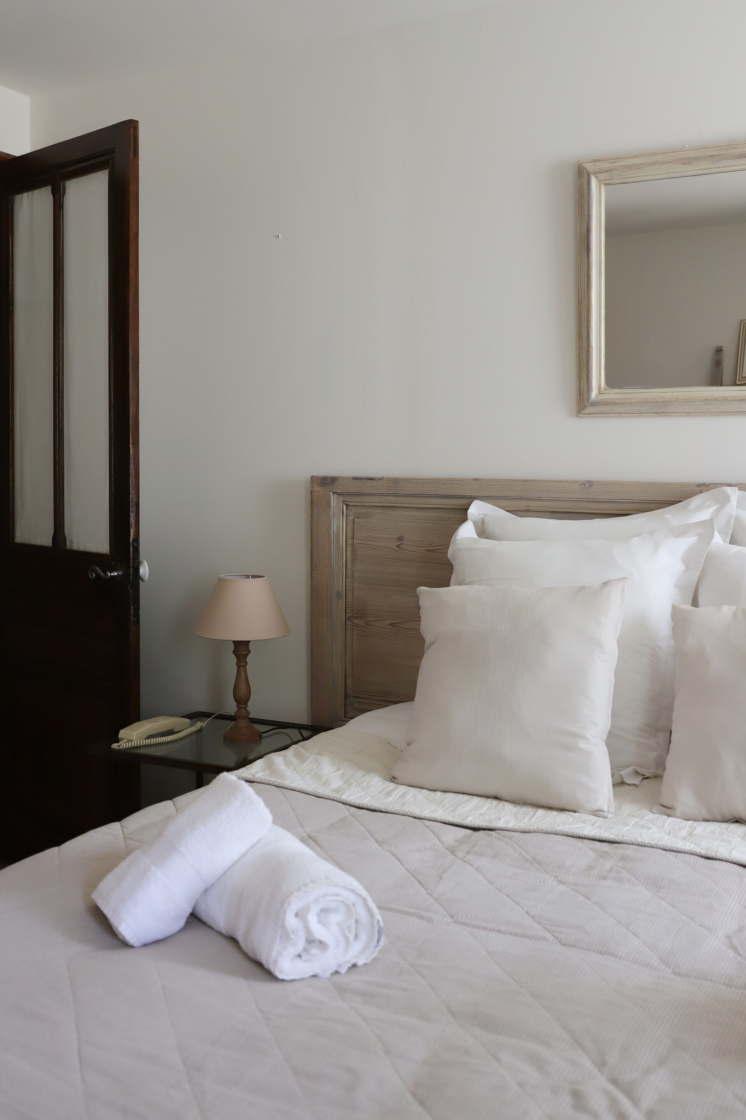 A neatly made bed with white bedding and pillows, a wooden headboard, a bedside lamp, and a telephone on a nightstand.